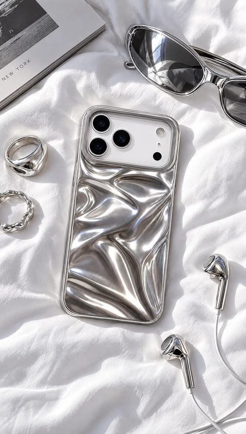 Chrome wave case on white sheets with silver sunglasses, rings and wired earbuds
